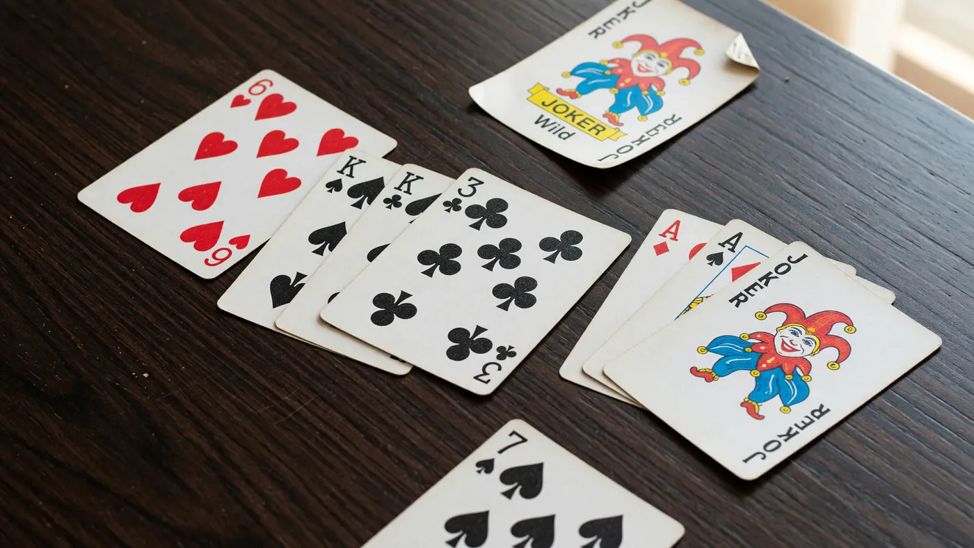 Four melds laid out on a dark wood surface with one open joker at the corner and a single loose card.