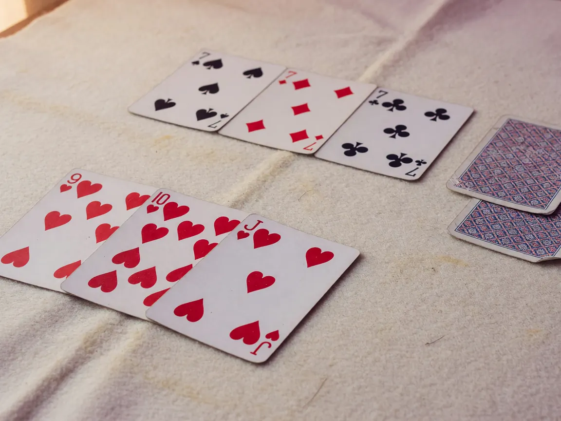 A rummy meld flatlay arranged on a worn cream felt surface: a clean pure sequence in the foreground, a second colour set behind it, two jokers turned face-down to the side, soft diffused daylight.